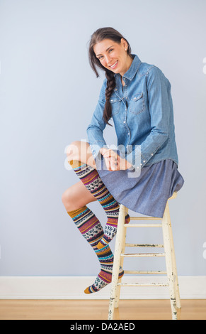 Studioaufnahme von Frau sitzt auf Schemel gestreifte Kniestrümpfen tragen Stockfoto