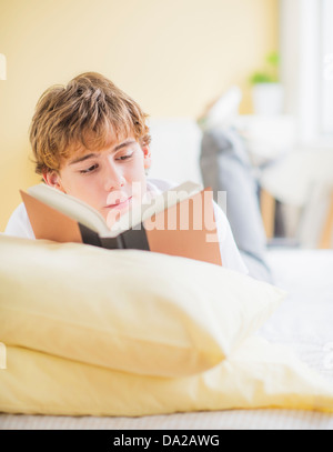 Teenager (14-15) auf Bett liegend und Buch Stockfoto