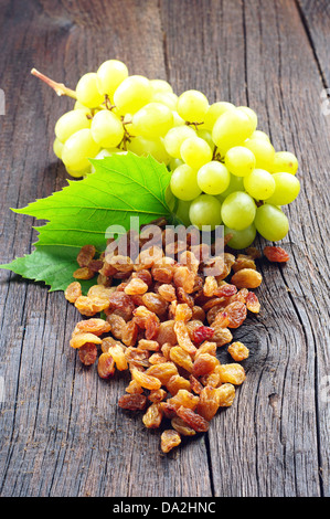 Rosinen und Weintrauben mit Blättern auf einem hölzernen Hintergrund Stockfoto