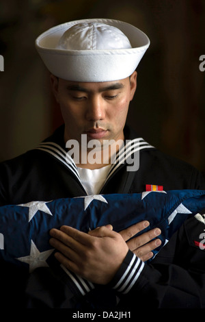 Ein US-Marine Seemann trägt die Flagge bei einer Seebestattung an Bord der San-Antonio-Klasse amphibious Transport dock Schiff USS Anchorage 13. Mai 2013 in Anchorage, AK. Stockfoto