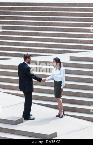 Ein kaukasischer Mann Geschäftsmann und eine asiatische Frau Geschäftsfrau Händeschütteln auf einen deal auf moderne Stadt Schritte stehen Stockfoto