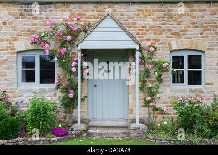 Cotswold Landhaus aus Stein mit rosa Rosen rund um die Tür. Icomb, Cotswolds, Gloucestershire, England Stockfoto