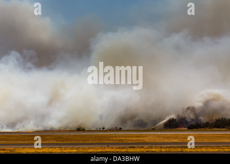 Feuerwehrleute feuchten die Bürste ab, als das Feuer am Ende der Start- und Landebahn am San Salvador International Airport schließt Stockfoto