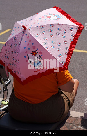 Frau Zuflucht von Sun unter Hello Kitty Regenschirm in Poole, Dorset im Juni Stockfoto