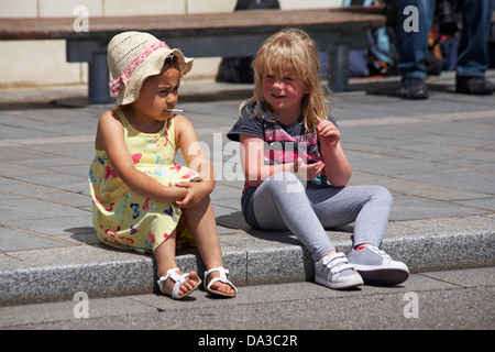 Zwei junge Mädchen sitzen auf Bürgersteig während Festivals in Poole im Juni Stockfoto