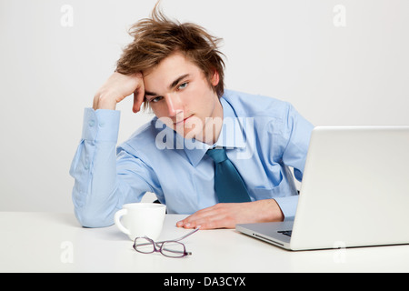 Erschöpften jungen Mann im Büro mit dem Laptop auf seiner Vorderseite Stockfoto