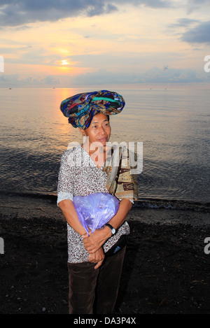 Eine balinesische Frau verkaufen Sarongs und Bett am Strand bei Sonnenuntergang deckt. Gegenstände sind auf dem Kopf transportiert. Stockfoto