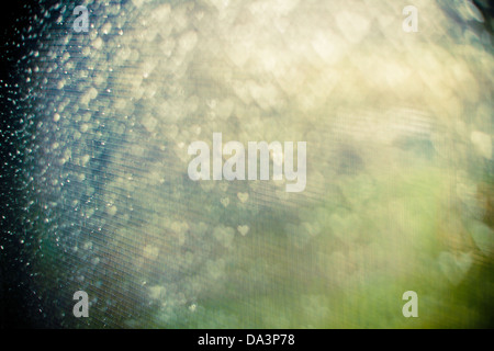 Regen-gesprenkelt Fenster übersät mit Bokeh Herzen in grün, gelb und blau-Tönen mit starker Vignettierung Stockfoto