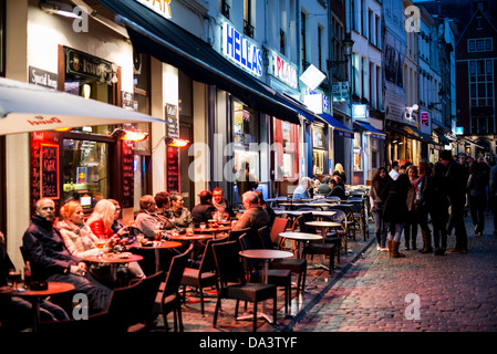 Gäste essen und trinken auf Sitzgelegenheiten im Freien vor einem Restaurant in der alten Stadt von Brüssel, Belgien, in der Nacht. Stockfoto