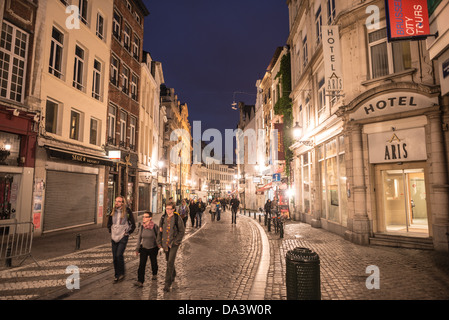 Touristen zu Fuß entlang einer Straße mit Kopfsteinpflaster in der unteren Stadt von Brüssel, in der Nacht. Stockfoto