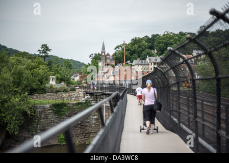 HARPERS Ferry Lower Town von Railroad Bridge Appalachian Trail Summer / HARPERS FERRY, West Virginia — Ein Fußgängerweg auf der umgestalteten CSX-Eisenbahnbrücke führt in Richtung Lower Town Harpers Ferry, wo der Turm der St. Peter's Roman Catholic Church und die Backsteinfassaden des historischen Viertels sichtbar sind. Der Appalachian Trail überquert hier den Potomac River und führt Fernwanderer direkt durch den Harpers Ferry National Historical Park – eine der bekanntesten Wanderorte auf der gesamten 2.190 Meilen (3.524 km) langen Route. Stockfoto