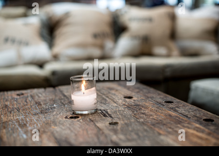 Eine kleine votive Kerze Ssits auf einem rustikalen Holztisch in einer Restaurantbar vor dem Sofa. Stockfoto