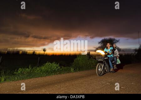 29. Juni 2013 - untergeht Battambang, Battambang, Kambodscha - ein Motorrad eine ländliche unbefestigte Straße auf den Sonnenuntergang über einem Reisfeld in der Nähe der Bamboo Train-Endstation in Battambang, Kambodscha. (Bild Kredit: Jack Kurtz/ZUMAPRESS.com ©) Stockfoto