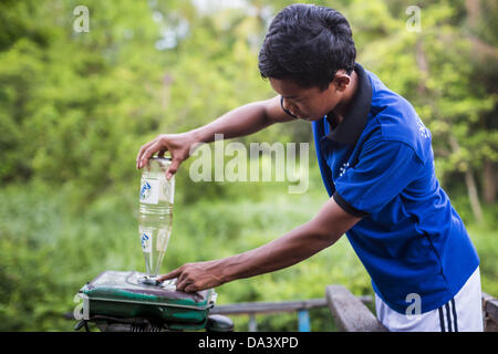 30. Juni 2013 - Battambang, Battambang, Kambodscha - legt ein Mann Gas in den Tank auf seine Bamboo Train in den Kopfbahnhof in der Nähe von Battambang. Der Bambus-Zug, ein Norry (Nori) in Khmer genannt ist einem 3m langen Holzrahmen, bedeckt in Längsrichtung mit Latten, die vom ultraleichten Bambus, das ruht auf zwei Langhantel-wie Drehgestelle, achtern derjenige durch Keilriemen zu einem 6HP-Benzin-Motor verbunden. Der Zug fährt auf Schienen, die ursprünglich von den Franzosen gelegt, als Kambodscha eine französische Kolonie war. Jahre des Krieges und Vernachlässigung haben die Bahnen für regelmäßige Züge unsicher gemacht.  Kambodschaner, die jeweils eine oder bis zu drei Tonnen 10 oder 15 Leute anziehen Stockfoto