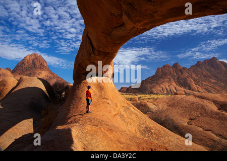 Junge unter natürlichen Felsen arch Spitzkoppe (links) und Pondok Berge in Ferne (rechts), Namibia, Afrika Stockfoto