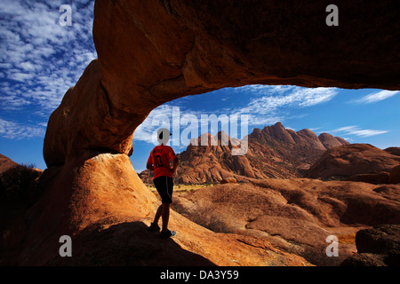 Junge unter natürlichen Felsbogen Spitzkoppe und Pondok Berge in Ferne, Namibia, Afrika Stockfoto