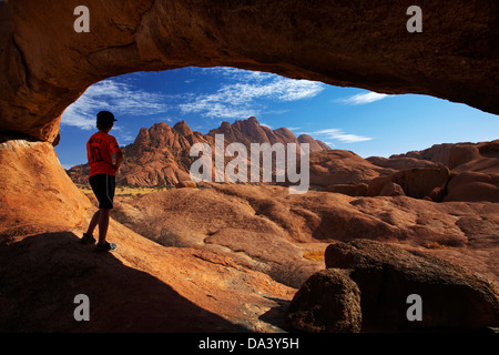 Junge unter natürlichen Felsbogen Spitzkoppe und Pondok Berge in Ferne, Namibia, Afrika Stockfoto