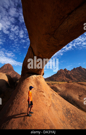 Junge unter natürlichen Felsen arch Spitzkoppe (links) und Pondok Berge in Ferne (rechts), Namibia, Afrika Stockfoto