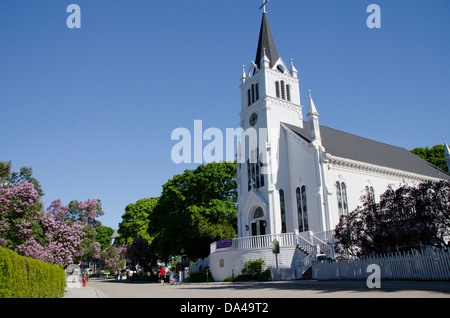 Michigan, Mackinac Island. Historische Sainte Anne Kirche mit blühenden Flieder Baum gesäumten Straße. Stockfoto