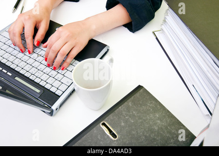 Nahaufnahme eines Womans Hände Tippen auf Laptop mit Ordnern und Becher Stockfoto