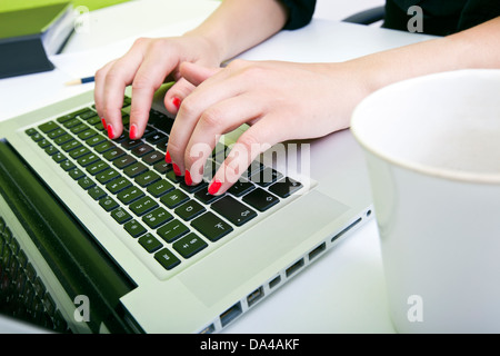 Nahaufnahme eines Womans Hände Tippen auf Laptop mit Becher im Vordergrund Stockfoto