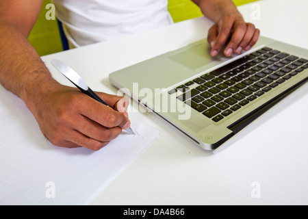 In der Nähe auf der indischen mans Hände schreiben auf Papier neben Laptop Stockfoto