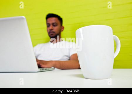 Indischen Mann arbeitet an seinem Schreibtisch mit Becher im Fokus im Vordergrund Stockfoto