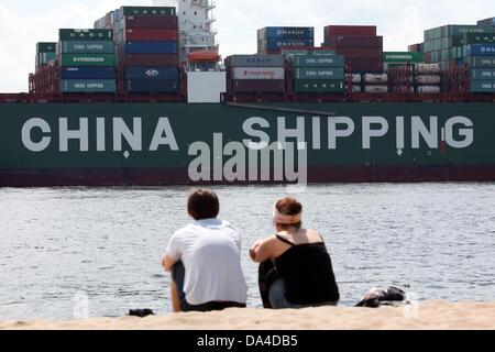 Tagesausflügler zusehen, wie das Containerschiff "CSCL Mars" von China Shipping Line betrieben Raftingboot auf der Elbe vom Ufer des Strandes Övelgönne in Hamburg, Deutschland, 3. Juli 2013 ist. Foto: BODO MARKS Stockfoto