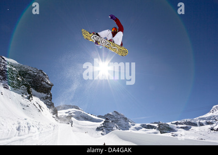SAAS-FEE, WALLIS, SCHWEIZ. Weiblichen Snowboarder fahren die Halfpipe mit einem Stalefish-Trick. Im Hintergrund die Sonne. Stockfoto