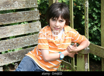 Porträt von Brünette Junge lächelnd auf sonnigen Holzbank im Garten Stockfoto