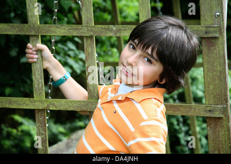 Brünette Junge stützte sich auf hölzernen Zaun im Garten Stockfoto