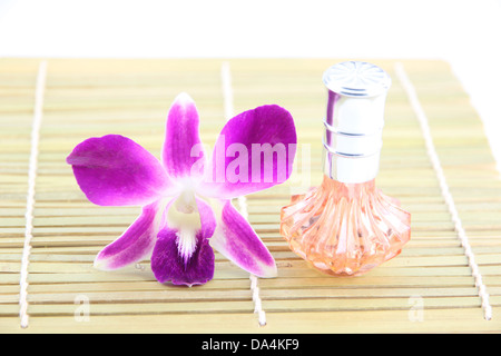 Lila Orchidee und Orange Parfüm Flaschen in Bambus Schale auf weißem Hintergrund. Stockfoto