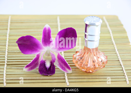 Lila Orchidee und Orange Parfüm Flaschen in Bambus Schale auf weißem Hintergrund. Stockfoto