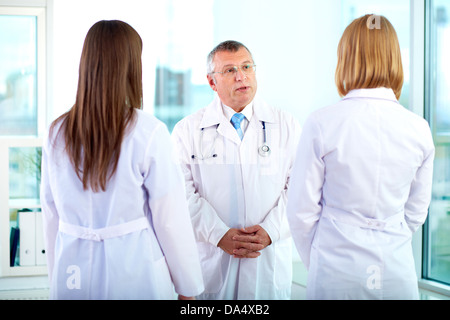 Porträt von Reifen Arzt im Gespräch mit einem der zwei junge Ärzte im Krankenhaus Stockfoto