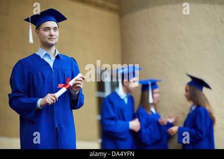 Freundlichen Studenten in Graduierung Kleider Interaktion mit nachdenklicher Kerl vor Stockfoto