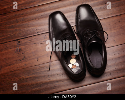 Nahaufnahme des Herrenschuhe auf dem Boden mit ändern Münzen im Inneren. Halten oder der Suche nach Geld an einer falschen Stelle Konzept. Stockfoto