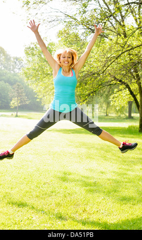 Glücklich weiblichen Fitness-Instruktor, springen, draußen im grünen Park trainieren Stockfoto