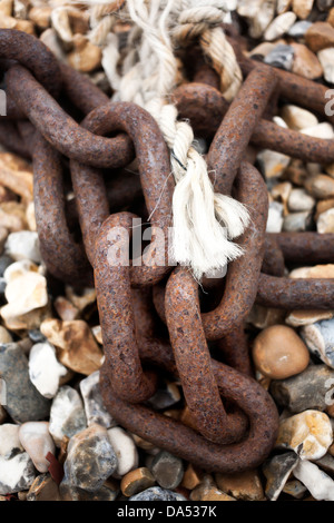 Detail des Links von rostigem Eisen Ankerkette und ausgefranste Seil ruht auf Kiesstrand Stockfoto