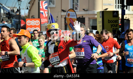 Läufer gekleidet als Clown bei den London Marathon Wellen auf die Menschenmenge inmitten einer Schar von anderen Läufern in Greenwich Stockfoto
