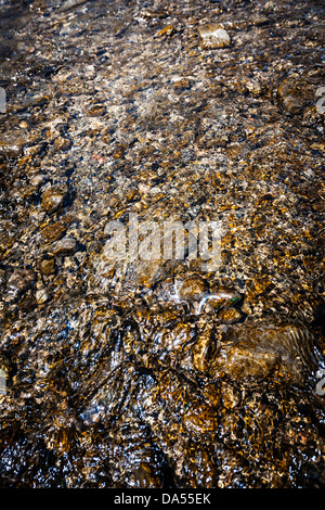 Saubere klare Wasser fließt über die glatten braunen Felsen Stockfoto