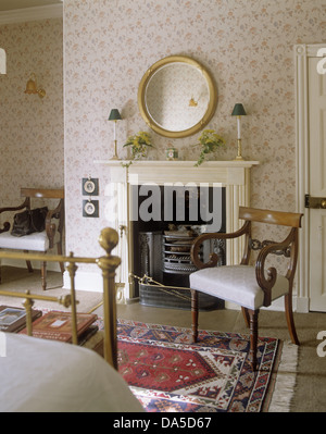 Antikes Holz Sessel am Kamin im Schlafzimmer mit Blumentapete und runder Spiegel Stockfoto