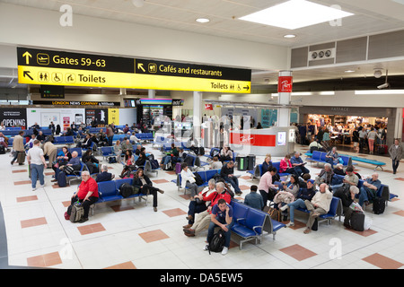 Reisende warten in Gatwick Flughafen Abflug-Lounge unter Wegweiser. Stockfoto