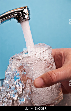 Wasser fließt aus einem Hahn in ein Glas. Stockfoto