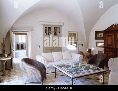 Graue Wicker Sessel und weißen Sofa gefliesten Kaffeetisch in weißen französischen Wohnzimmer mit Fliesenboden und gewölbte Decke Stockfoto