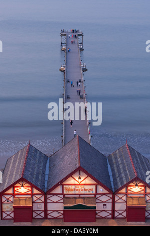 Sommerabend hoch über beleuchtete Eingang Kioske & Menschen zu Fuß auf Saltburn pier über ruhigen Nordsee - Saltburn-by-the-Sea, England, UK. Stockfoto