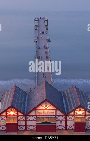 Sommerabend hoch über beleuchtete Eingang Kioske & Menschen zu Fuß auf Saltburn pier über ruhigen Nordsee - Saltburn-by-the-Sea, England, UK. Stockfoto