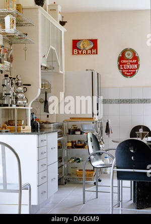 Metall-Tisch und Stühle im Zentrum der modernen Küche mit freistehenden Lagereinheit und fünfziger Jahre Werbung an der Wand Stockfoto