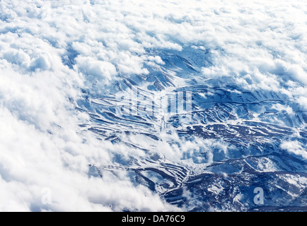 Vogelperspektive auf verschneite Berge, Szene auf dem Berg durch weiße flauschige Wolken, Winterurlaub, kaltem Wetter Stockfoto