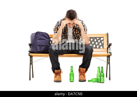 Junger Mann mit Kater sitzt auf einer Bank, leere Bierflaschen auf dem Boden Stockfoto