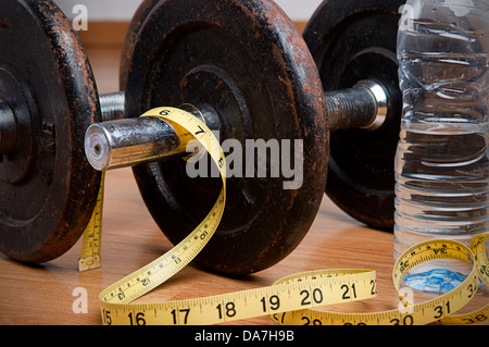 Paar Hanteln, Klebeband und eine Flasche Wasser zu messen. Bewegung und gesunde Ernährung Konzept. Stockfoto
